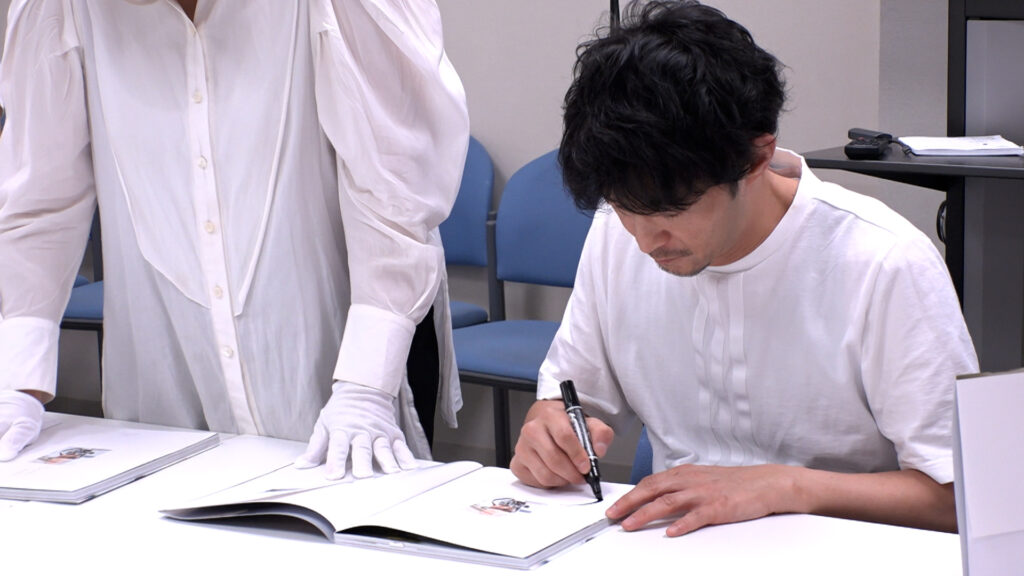Kenjiro Tsuda signing printed copies of his “Whisper” photobook